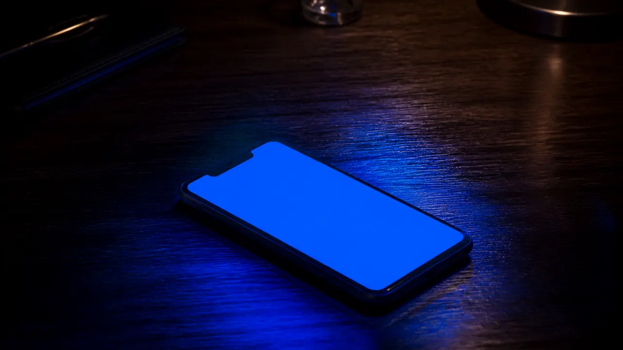 Phone in a dark room filling the wooden desk with a solid blue glow, no letters or logos