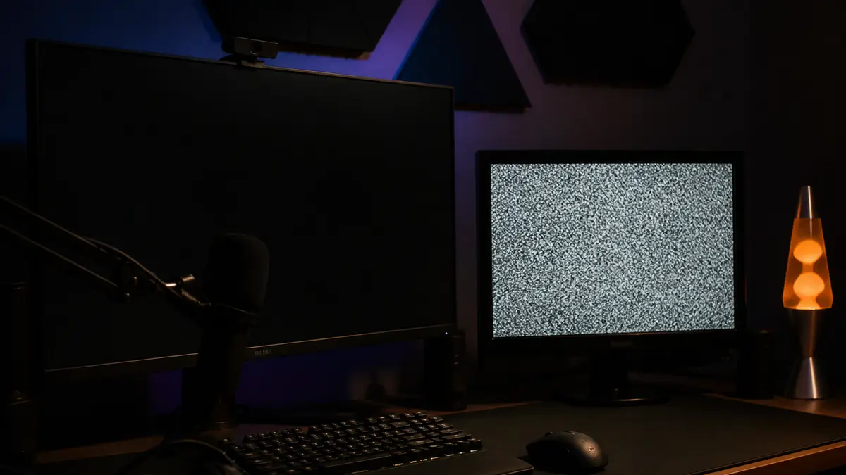A streaming desk with two monitors, one glowing with grainy TV snow, no interface labels. Capture the browser window for a silent break scene.